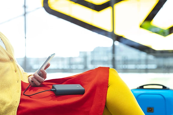 Uma pessoa senta-se na área de espera de um aeroporto e carrega o seu smartphone com um powerbank da Hama.