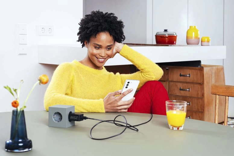 Jovem mulher sentada à mesa com o carregador rápido da Samsung e a sorrir para o seu smartphone.
