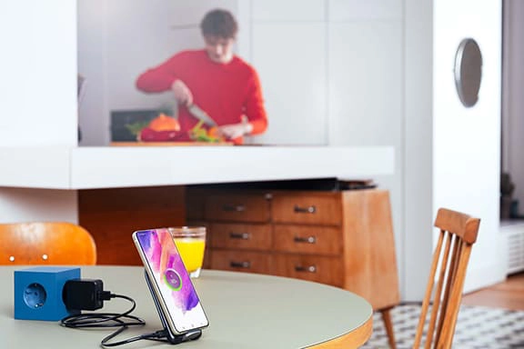 Um adolescente cozinha ao fundo enquanto um smartphone da Samsung carrega na estação de carregamento por indução.